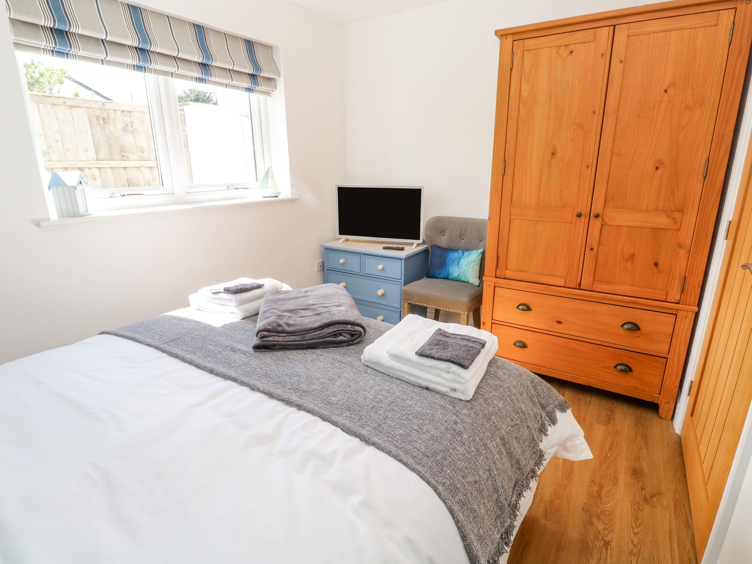 A bedroom with a bed, a wooden wardrobe, a television, and a window with blinds.