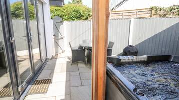 A patio area with a glass door leading to a covered outdoor space, a small table with chairs, and a hot tub.