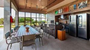 Una cocina moderna al aire libre con una larga mesa de comedor y sillas, un protector contra salpicaduras de ladrillo y electrodomésticos de acero inoxidable.