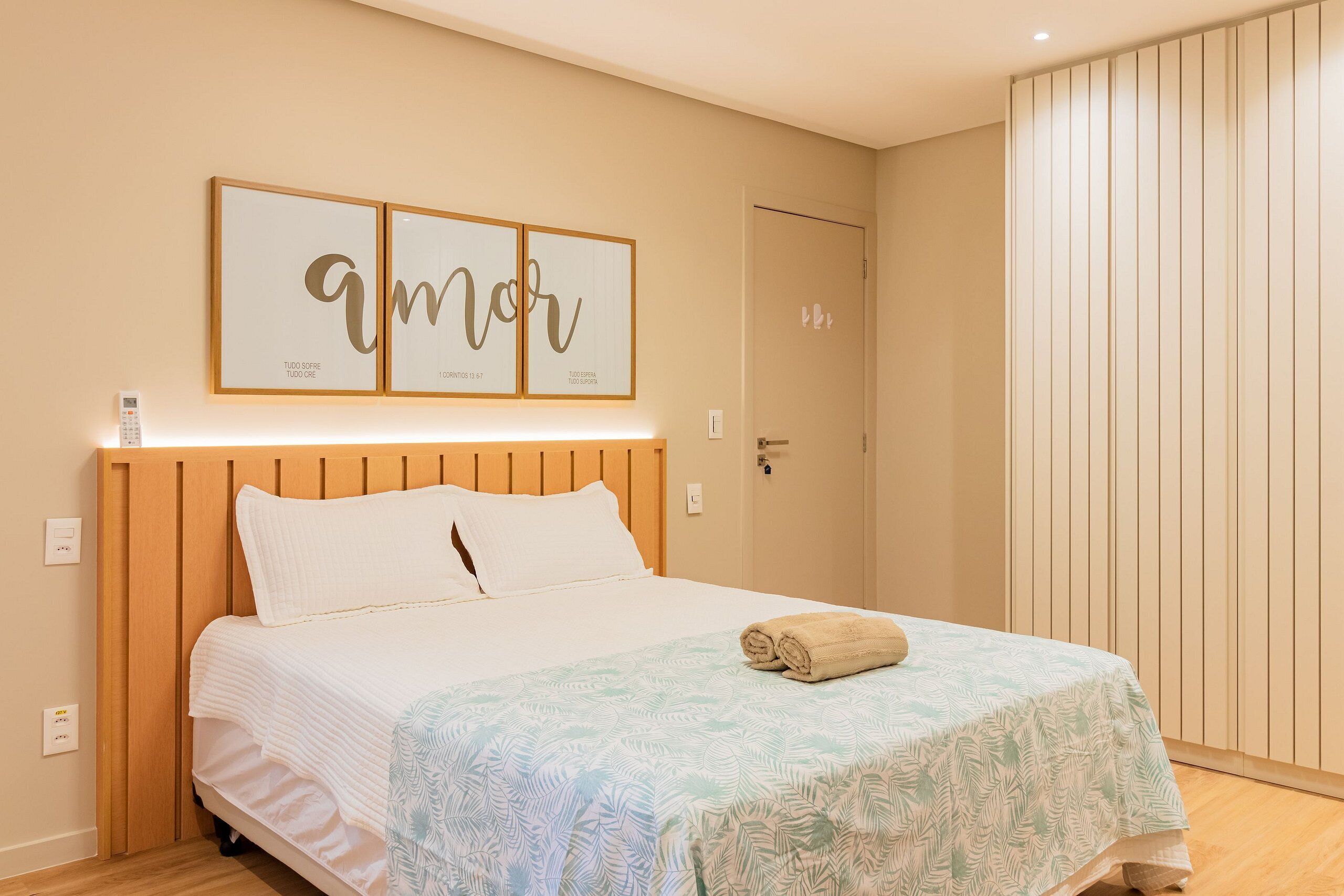 A neatly made bed with a patterned bedspread, a wooden headboard, and two framed motivational quotes on the wall above.