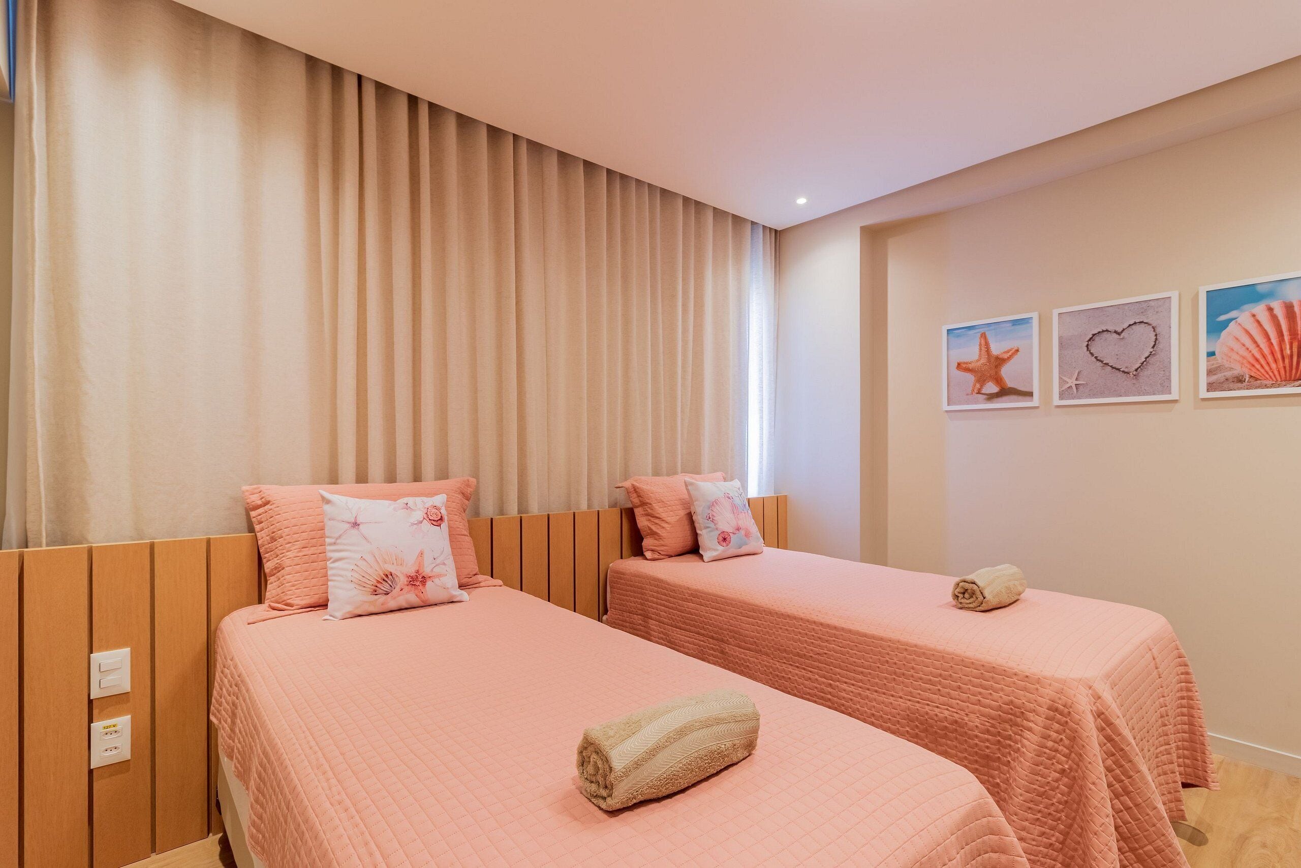A hotel room with two beds, beige curtains, and wall art including a starfish and a heart.