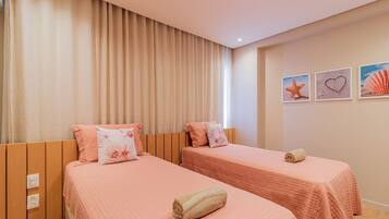 A hotel room with two beds, beige curtains, and wall art including a starfish and a heart.