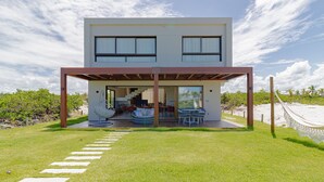 Una casa moderna de dos pisos con un porche cubierto, una escalera que lleva al nivel superior y vista a la playa.