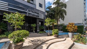 A modern building with a pool, potted plants, and a landscaped area with a curved pathway. - Praca Benedito Calixto - Duplex (São Paulo)