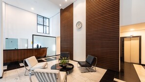A modern reception area with a reception desk, two seating areas with chairs, a clock on the wall, and a large window. - Praca Benedito Calixto - Duplex (São Paulo)