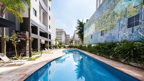 A swimming pool with lounge chairs, surrounded by buildings and greenery. - Praca Benedito Calixto - Duplex (São Paulo)