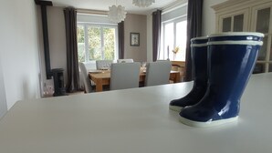 A dining area with a table set for four, a window with curtains, and a pair of blue boots on a white table. - Waterfront villa with panoramic sea view (Logonna-Daoulas)