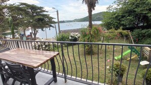A balcony with a wooden table and chairs, overlooking a body of water with boats and greenery. - Waterfront villa with panoramic sea view (Logonna-Daoulas)
