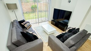 Een moderne woonkamer met een grijze zithoek, een witte salontafel en een flatscreen televisie.
