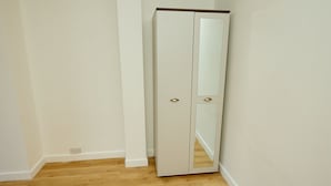 Een witte garderobe met twee deuren en een spiegel, geplaatst in een hoek van een kamer met houten vloer.