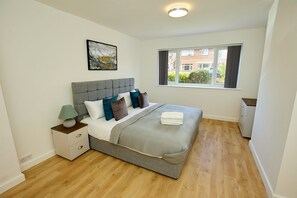 A bedroom with a bed, nightstand, lamp, and a window with a view of buildings. - Charming 5-bedroom House in the Heart of Bexley (Bexley)