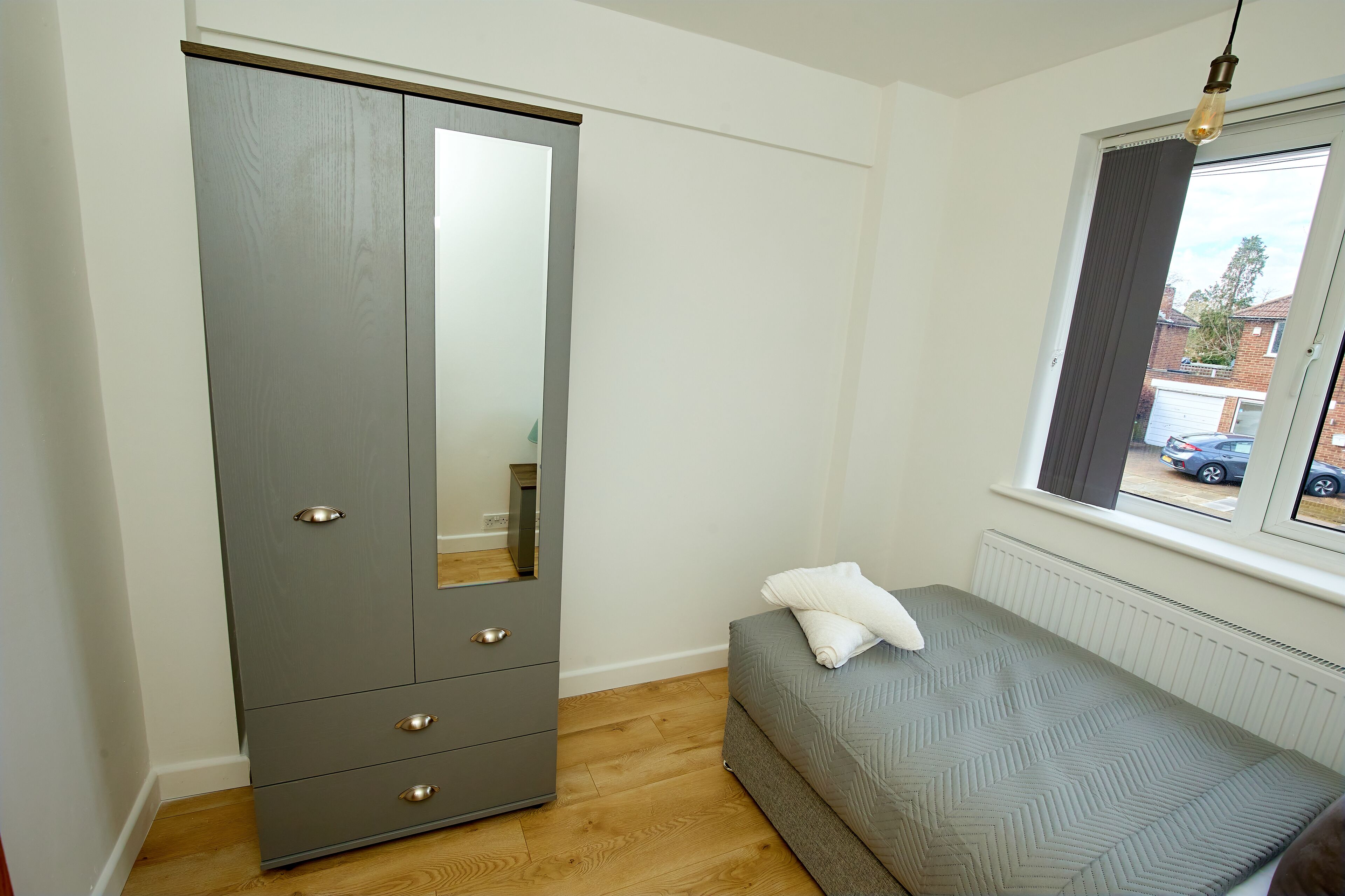 Une chambre avec une armoire grise, un lit avec un matelas gris et une fenêtre donnant sur l’extérieur.