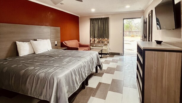 A hotel room with a large bed, a desk, a chair, a TV, and a view of the outdoors. - Hollywood Inn (Houston)