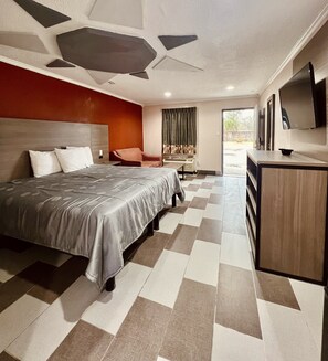 Een hotelkamer met een groot bed, een bureau, een stoel, een televisie en uitzicht op het omliggende landschap.