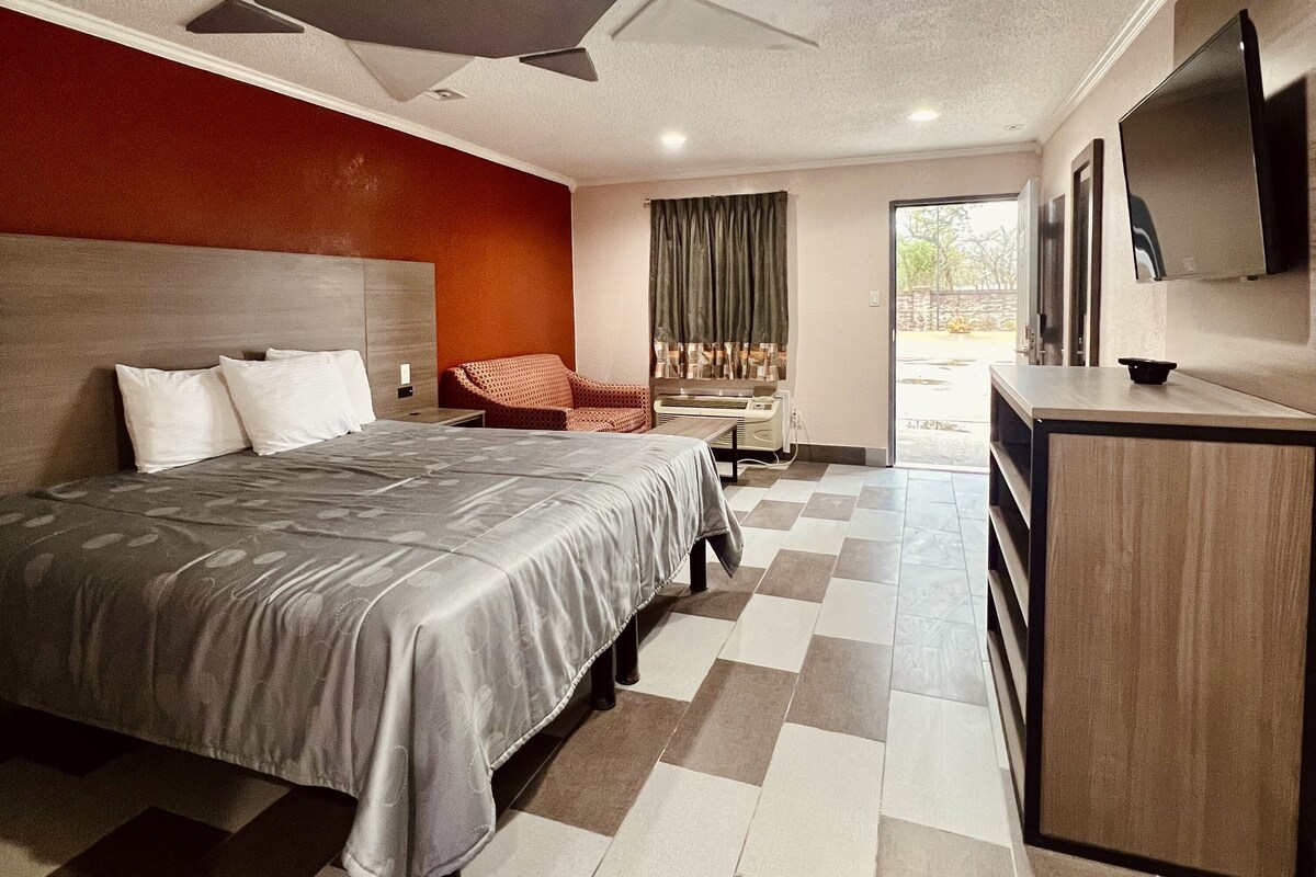 A hotel room with a bed, a chair, a desk, a television, and a view of the outside.