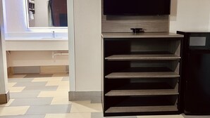 A modern living room with a flat-screen TV mounted on a wooden shelf, a built-in bench, and a view of a bathroom through an arched doorway. - Hollywood Inn (Houston)