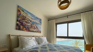 Une chambre à coucher avec un lit, un tableau, une fenêtre donnant sur un beau paysage et un luminaire suspendu.