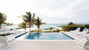Une piscine bordée de chaises longues, de palmiers, et offrant une vue sur la plage et l’océan.