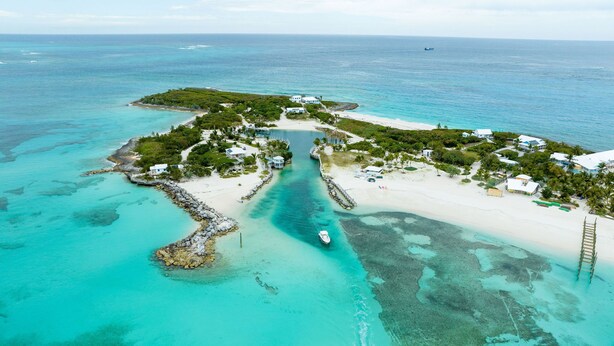 Vue aérienne d’une île tropicale aux eaux turquoise et limpides, avec une plage de sable blanc et un petit bateau ancré près du rivage.