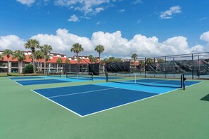 A tennis court with a net, surrounded by a fence, and palm trees in the background. - Beachfront Days Ocean View Condo Bliss (Panama City Beach)