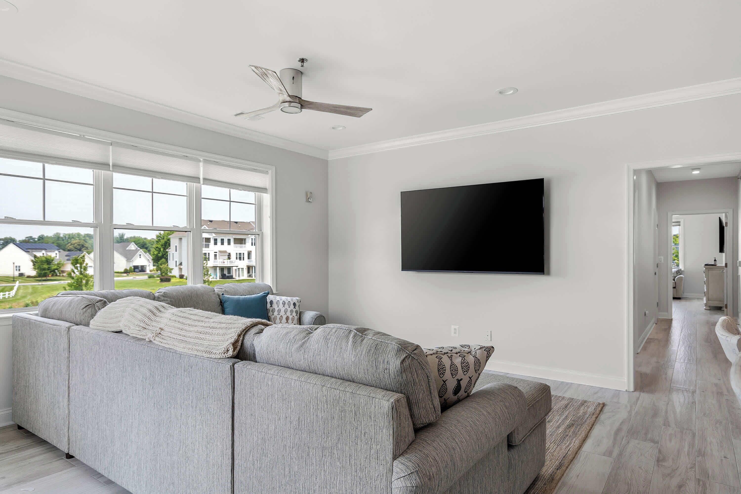 Una sala de estar moderna con un sofá modular, un televisor de pantalla plana montado en la pared y un ventilador de techo.