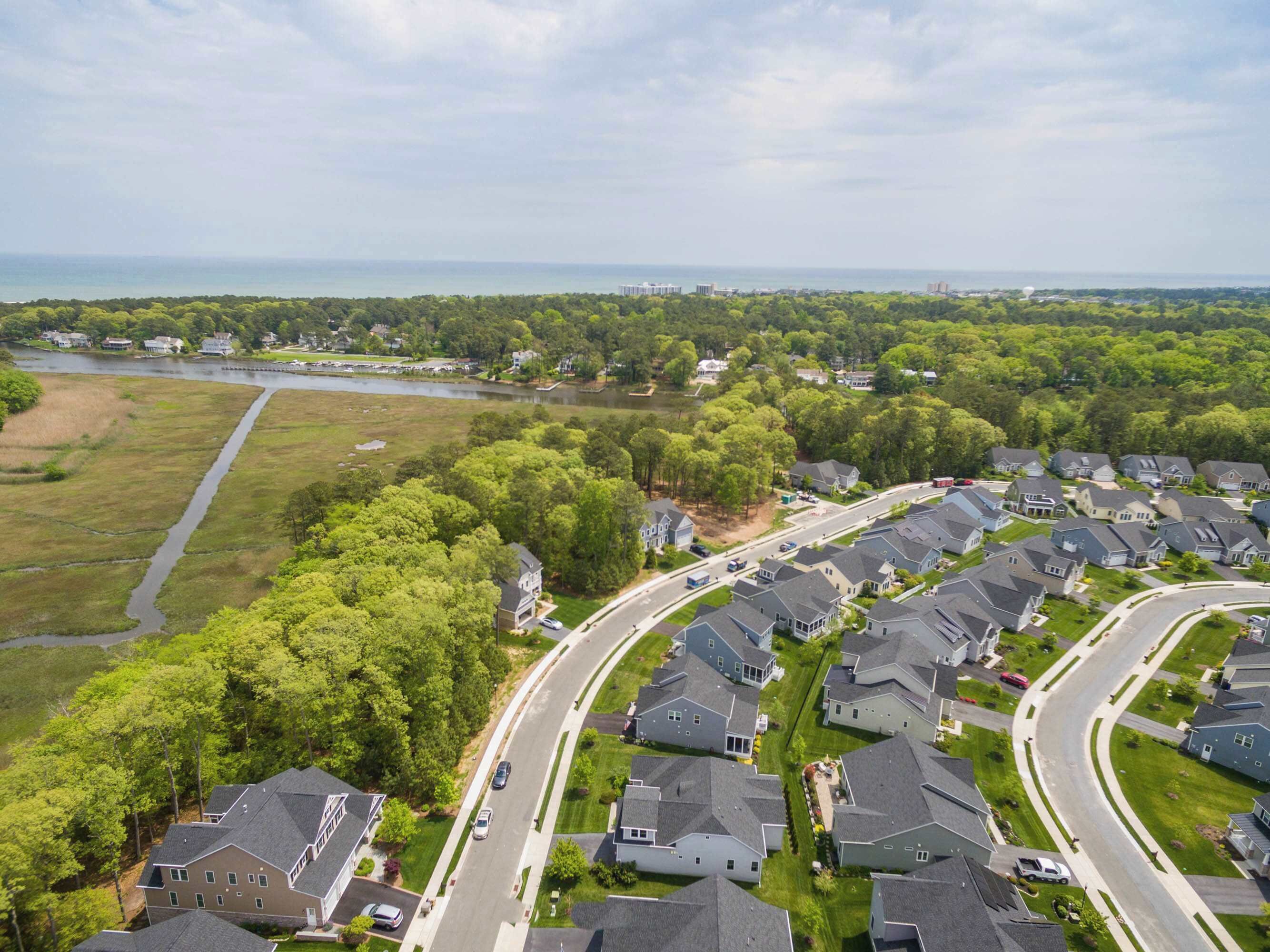 Un quartier résidentiel où les maisons sont disposées le long d’une rue sinueuse, entouré de verdure et bordé par un plan d’eau.