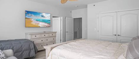 A bedroom with a large bed, a ceiling fan, a dresser, and a painting of a beach scene.