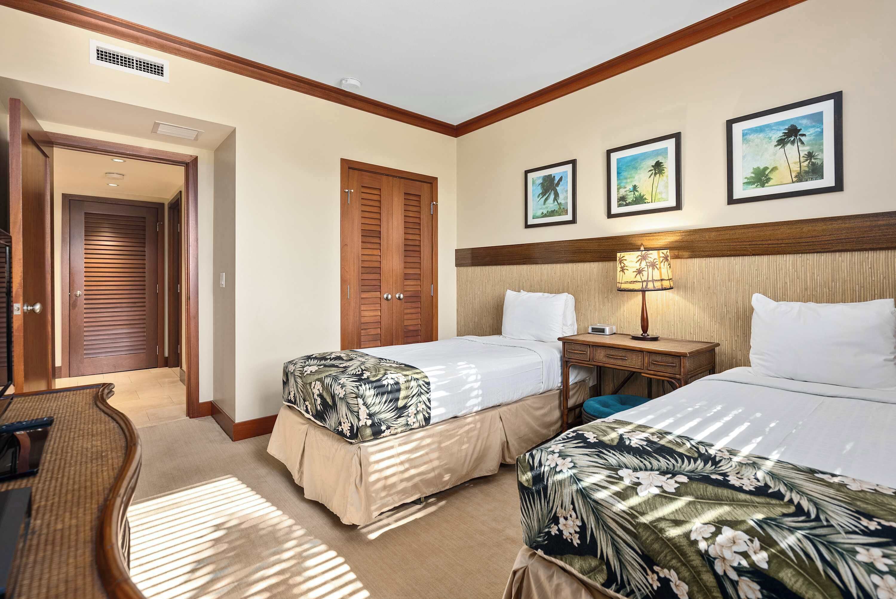 Habitación de hotel con dos camas, cabecera de madera, mesita de noche, lámpara y puerta que da a otra habitación.