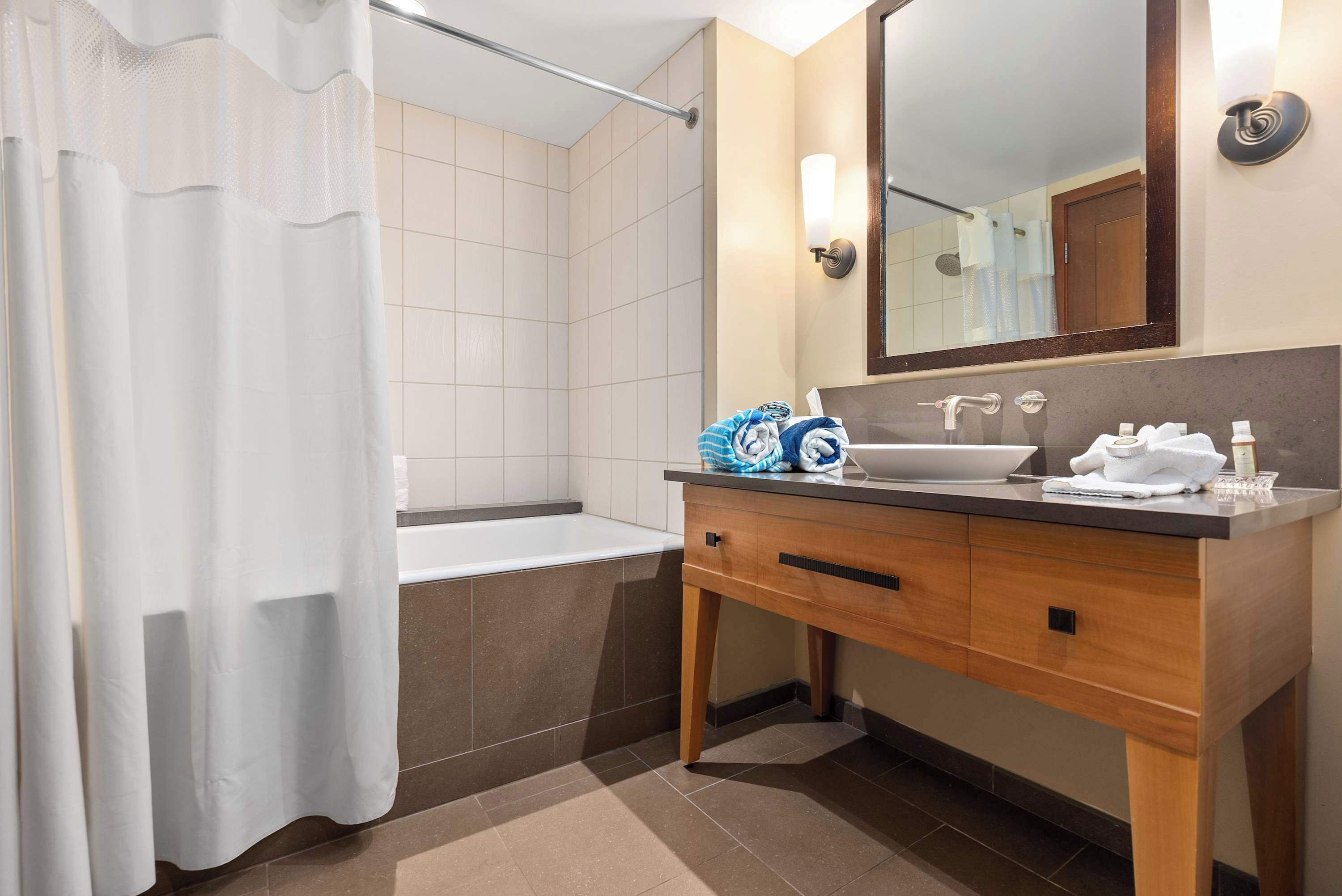 Une salle de bain moderne avec une baignoire, un lavabo surmonté d’un grand miroir et un meuble-lavabo en bois doté de tiroirs.
