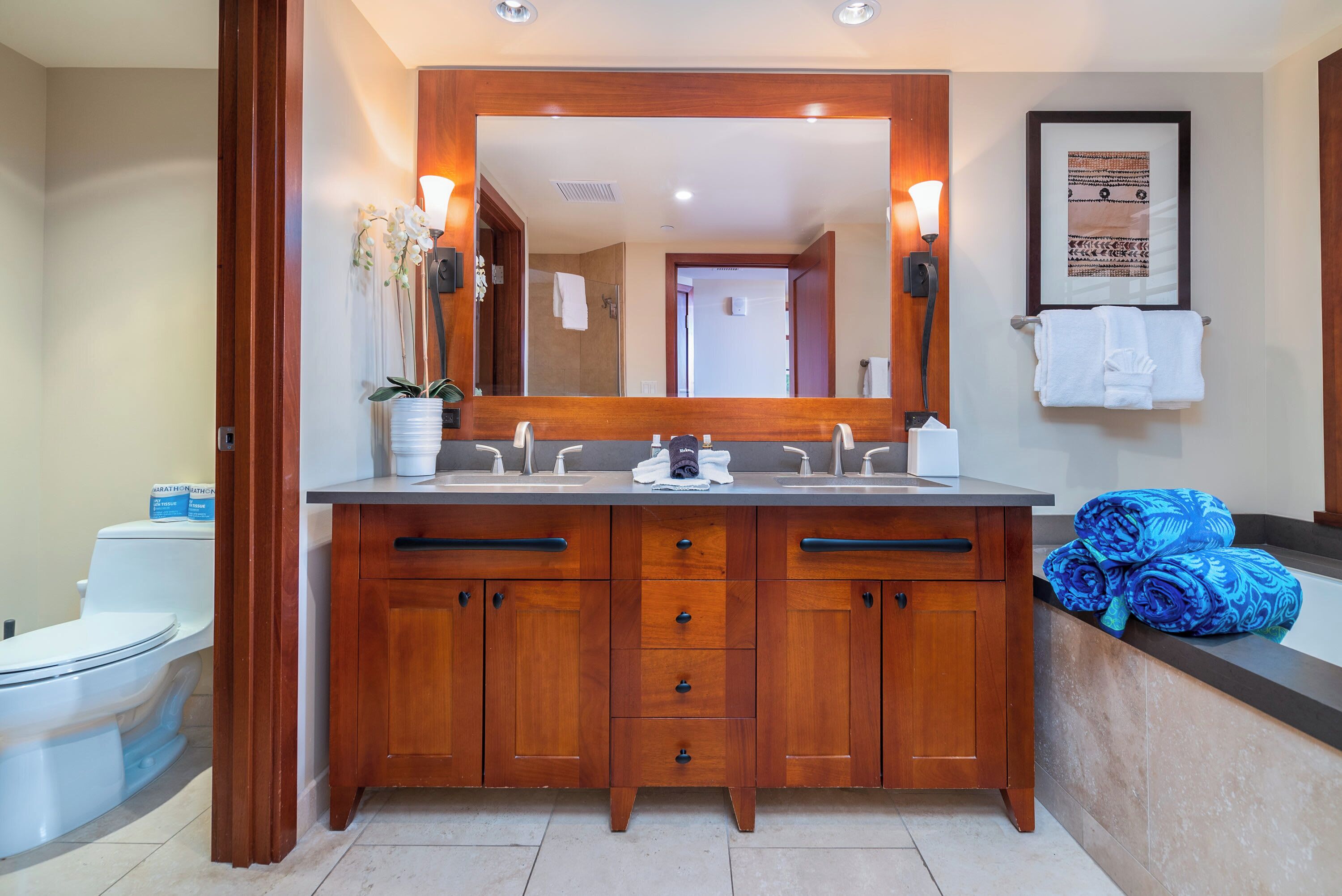 A bathroom with a wooden vanity, a large mirror, and a framed picture on the wall.