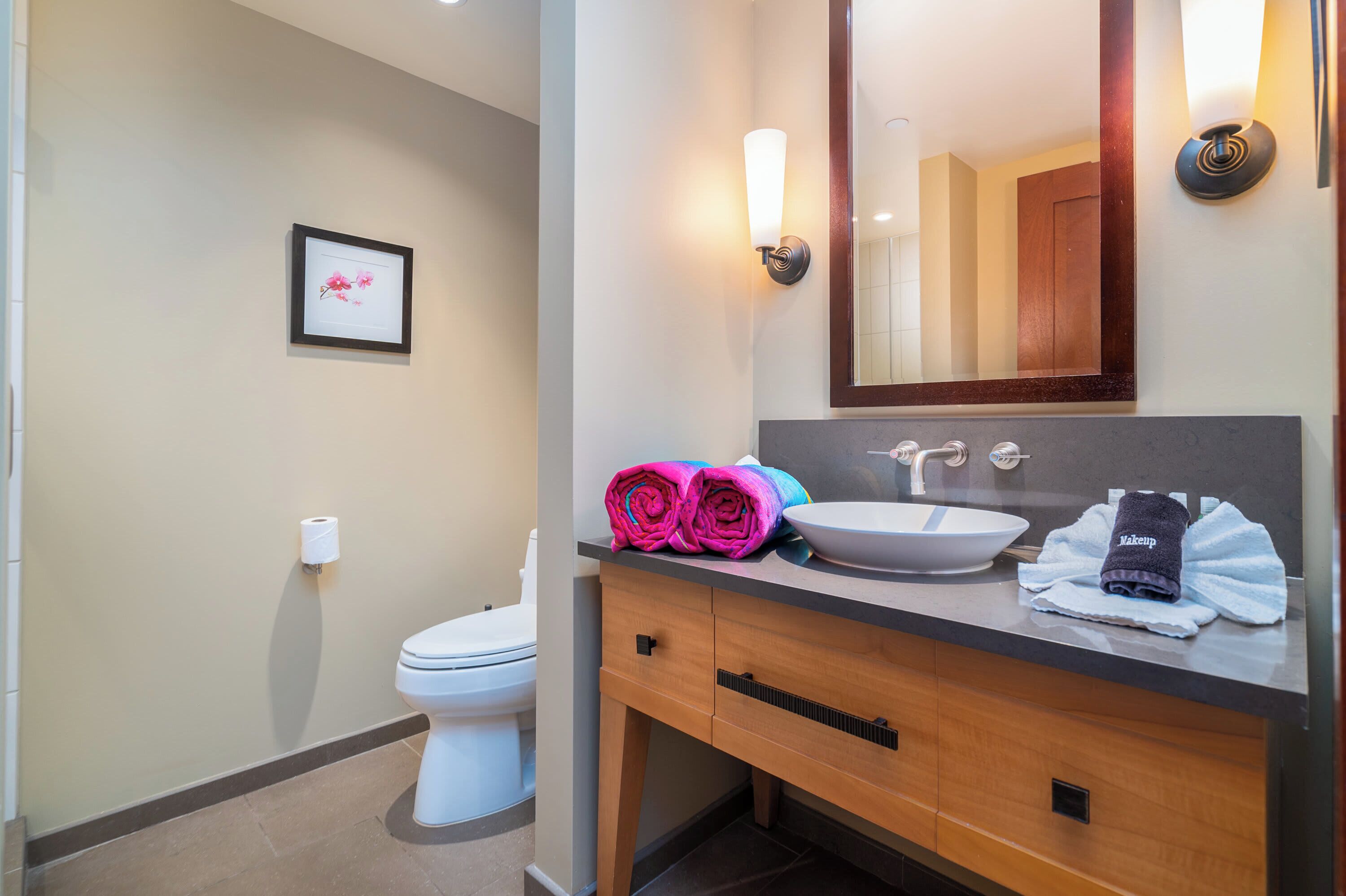Un baño moderno con lavabo blanco, tocador de madera y un espejo grande.