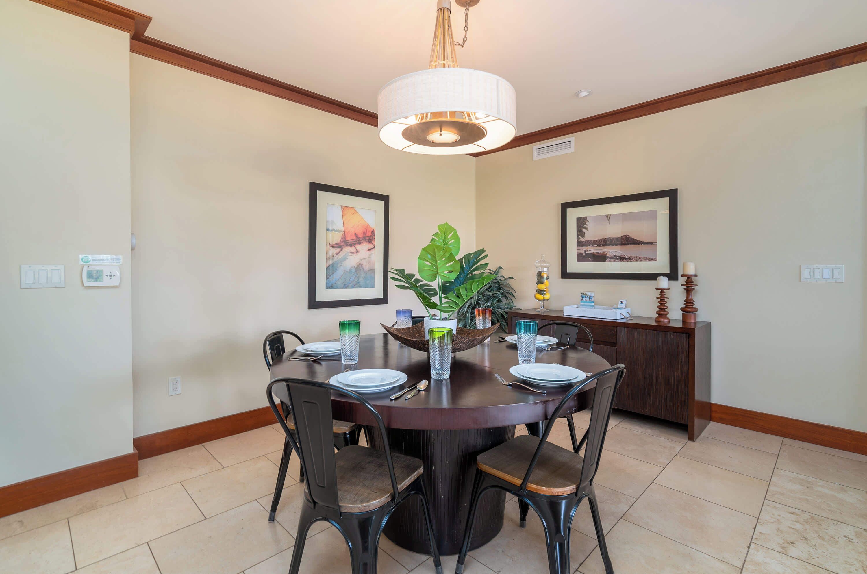 A dining area with a round table, chairs, a chandelier, framed artwork, and a plant centerpiece.