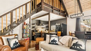 Una sala de estar acogedora con un sofá de cuero marrón, un sofá beige y una escalera de madera.