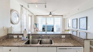 A modern kitchen with granite countertops, a double sink, and a view to the outside. - Sunset Shores Oceanfront Condo Bliss (Panama City Beach)