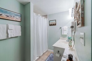 A bathroom with a shower curtain, a sink, a towel rack, and a sign that reads "B&B HOUSE".