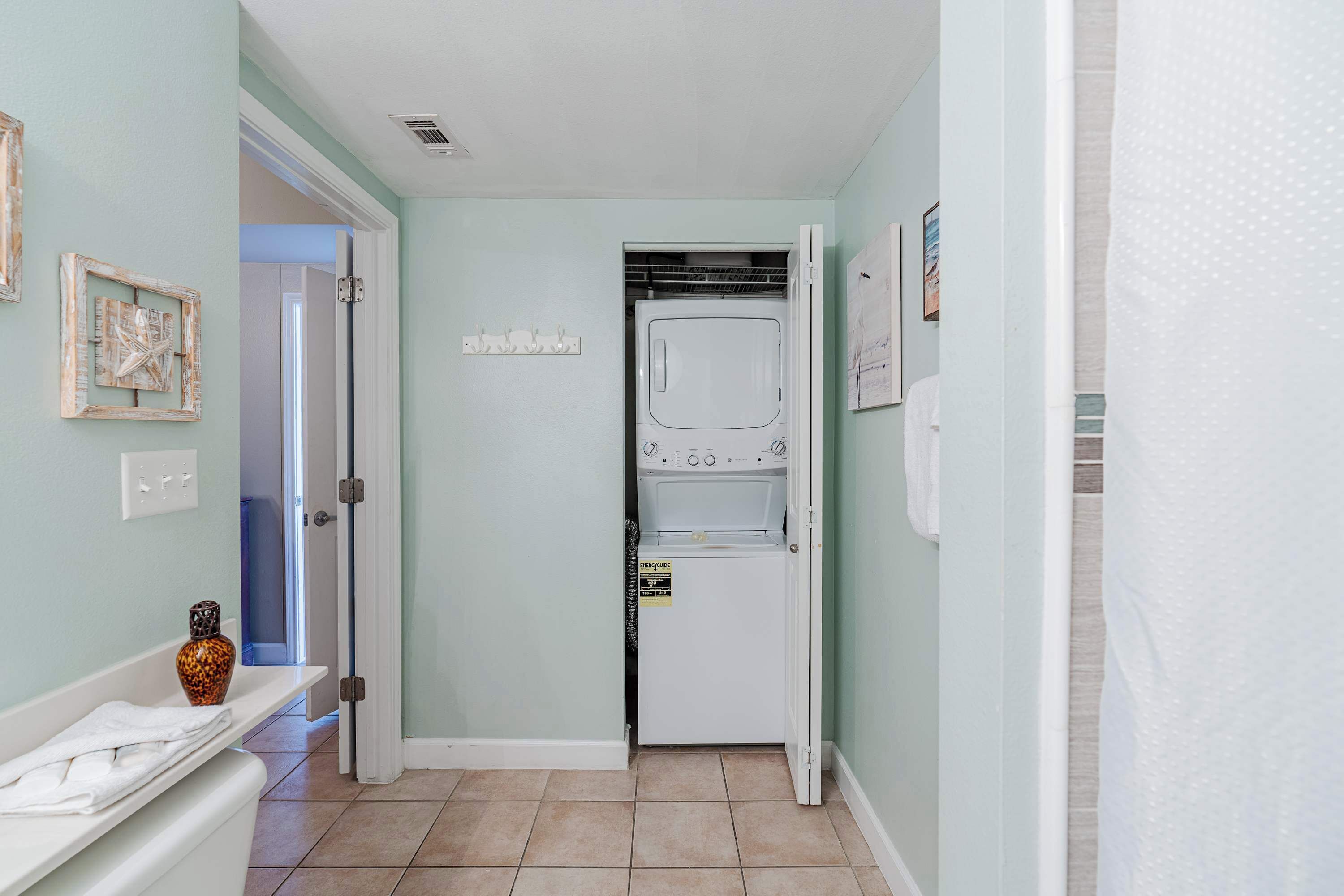 A laundry room with a front-loading washer and dryer, a wall-mounted drying rack, and a door leading to another room.