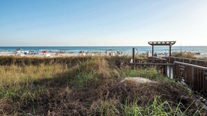 A beach with a wooden boardwalk leading to a covered area, sandy beach, and clear blue sky. - Sunset Shores Oceanfront Condo Bliss (Panama City Beach)