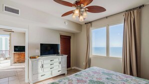 A bedroom with a bed, a television, a dresser, and a window with curtains. - Sunset Shores Oceanfront Condo Bliss (Panama City Beach)