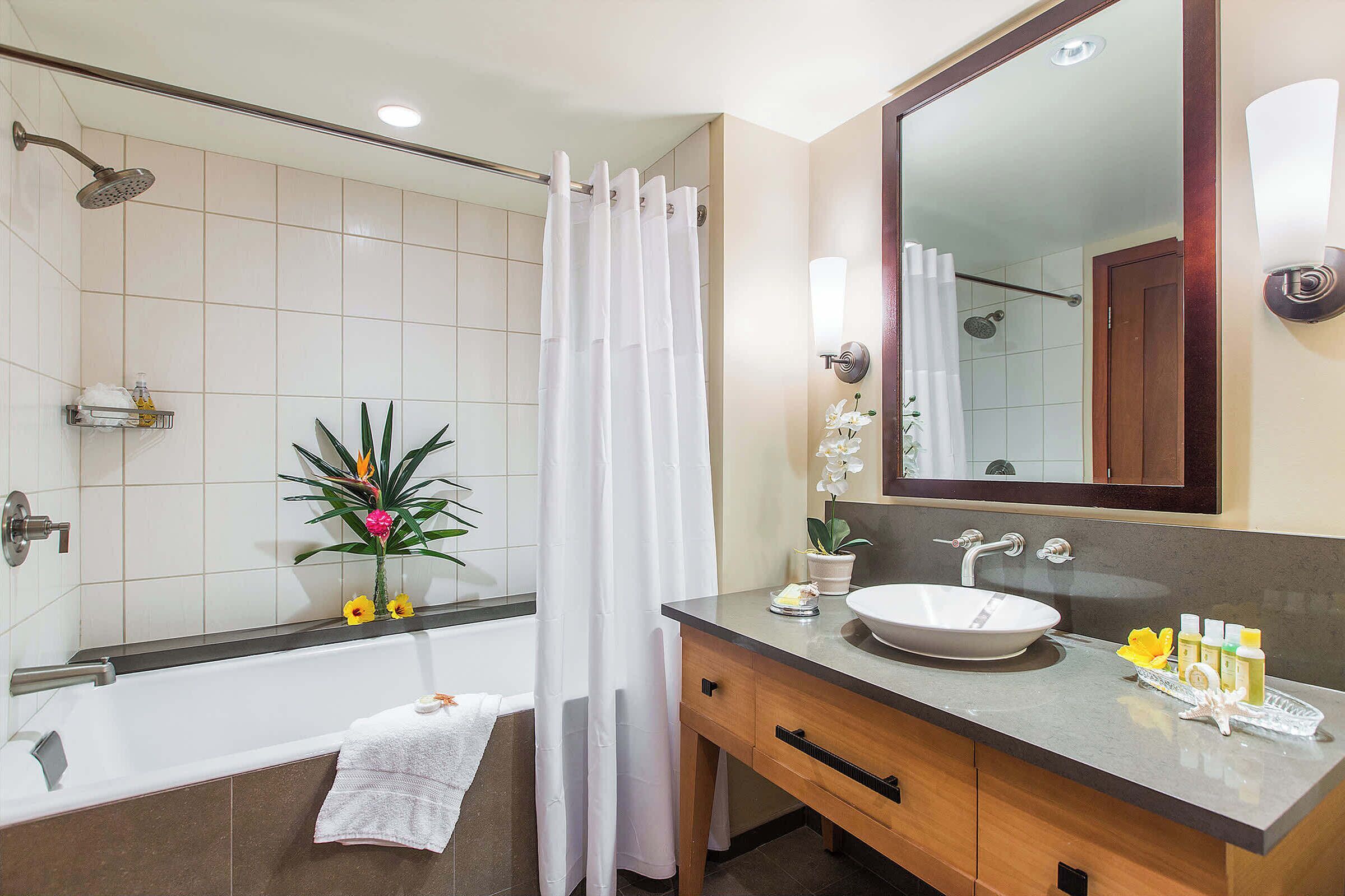 A bathroom with a bathtub, a sink, and a mirror. There is a shower curtain, a towel, and a plant on the counter.