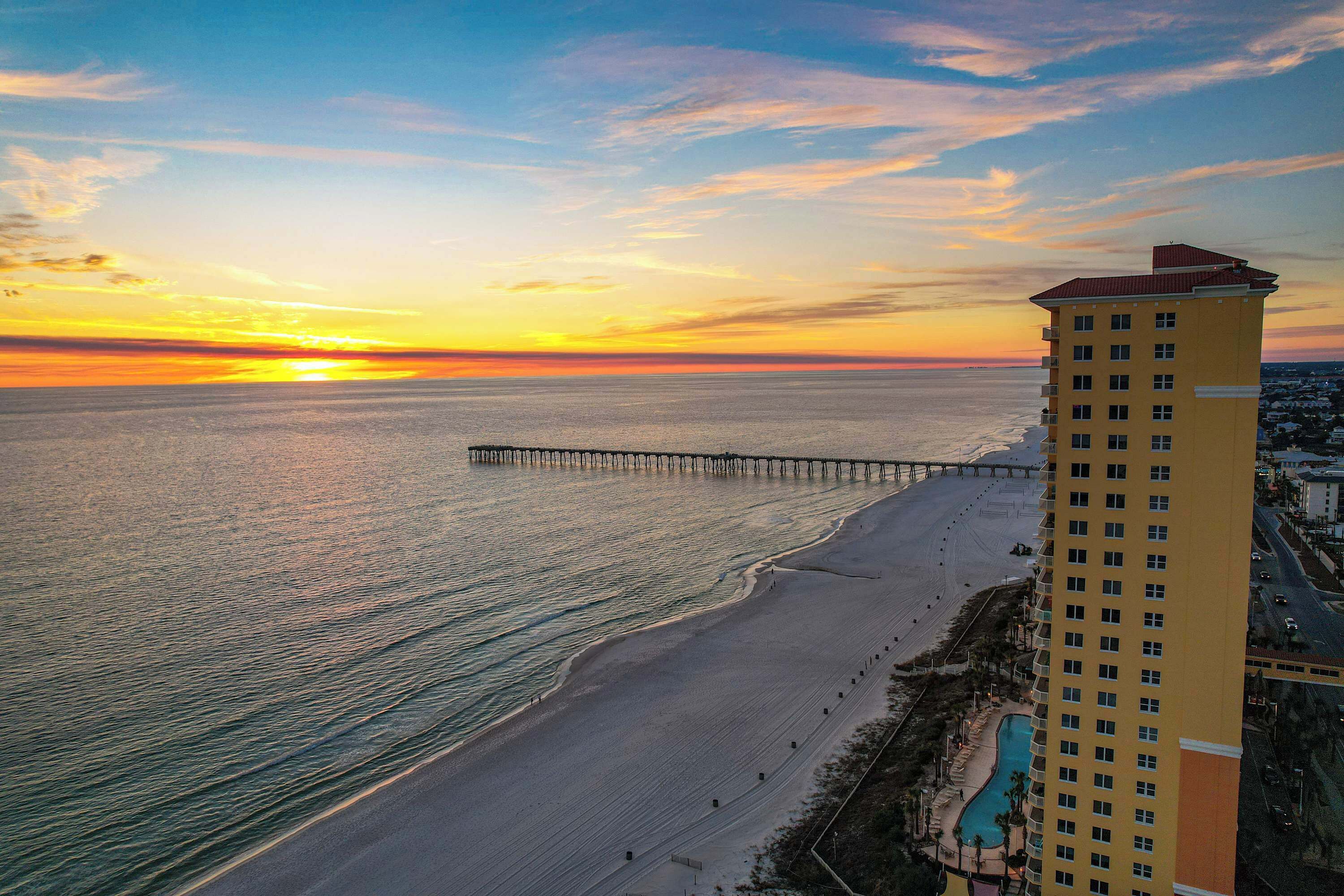 A high-rise hotel with a beach view, a pier extending into the ocean, and a swimming pool.