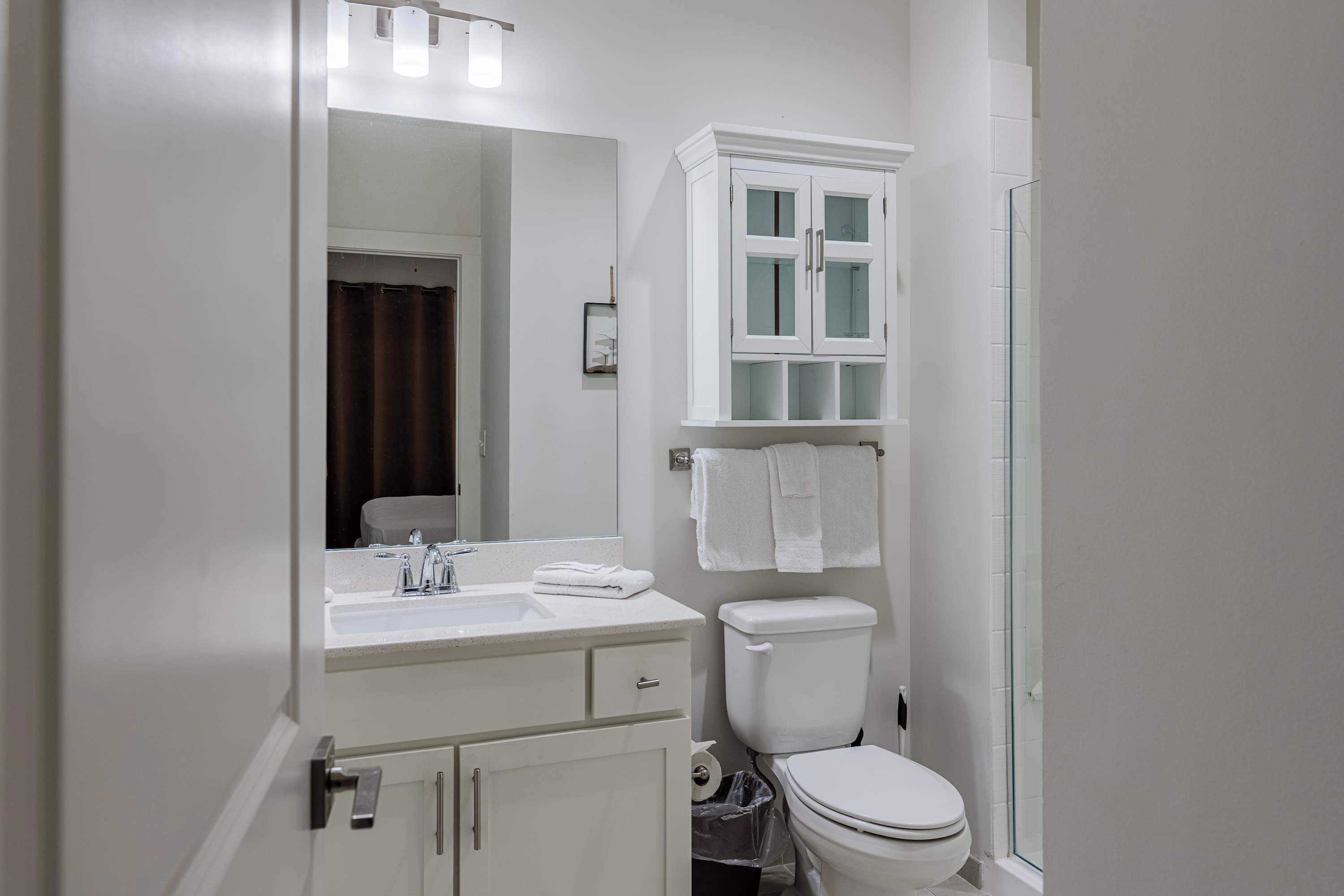 A bathroom with a white sink, mirror, cabinet, toilet, and glass shower enclosure.