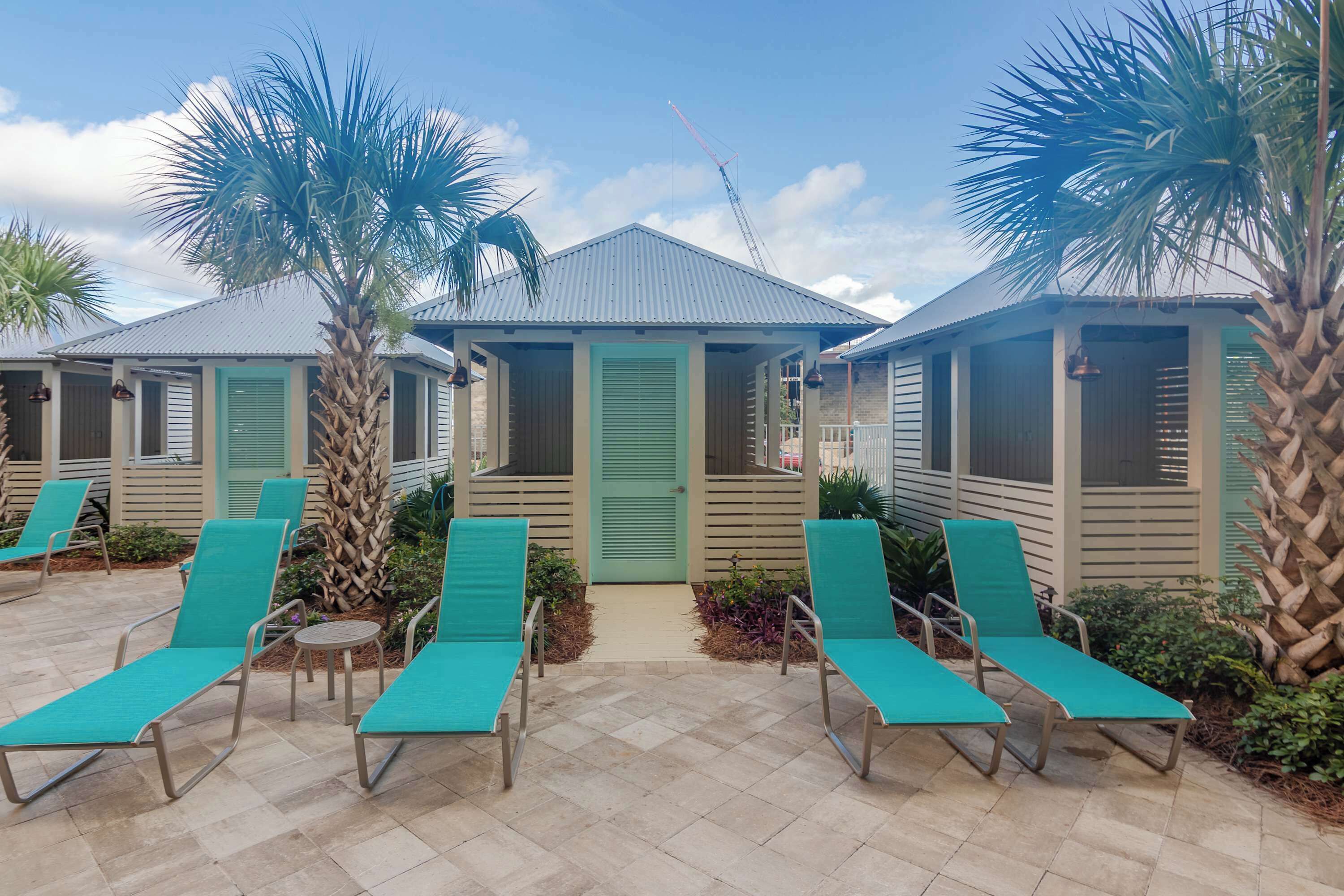 A row of beachside cottages with green shutters, a tiled patio, and lounge chairs.