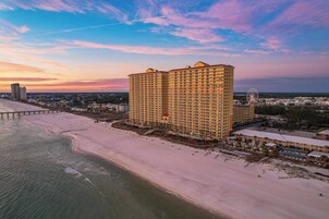 A high-rise hotel with multiple floors, a beach in the foreground, and a pier extending into the water.