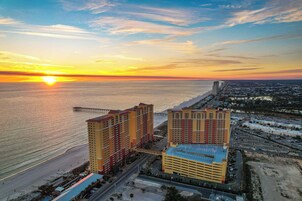 A high-rise hotel with multiple floors, a parking lot, and a beach view.