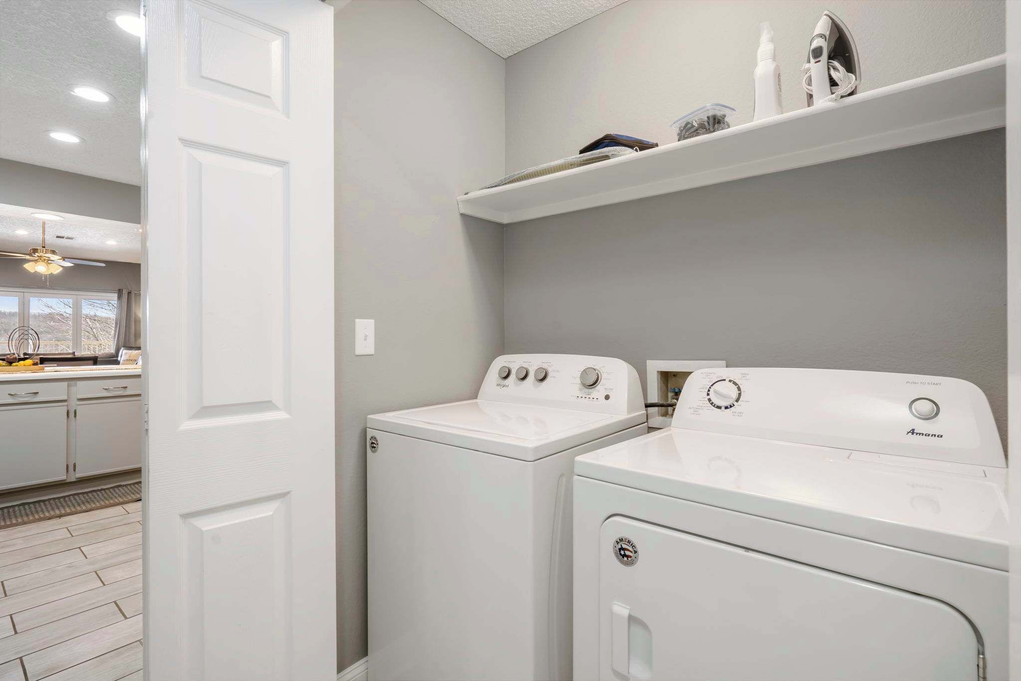 A laundry room with two white front-loading washers and dryers, a ceiling fan, and a shelf above the dryers.
