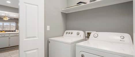 A laundry room with two white front-loading washers and dryers, a ceiling fan, and a shelf above the dryers.