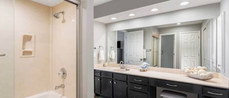 A modern bathroom with a bathtub, a shower, a vanity with a large mirror, and a sink.