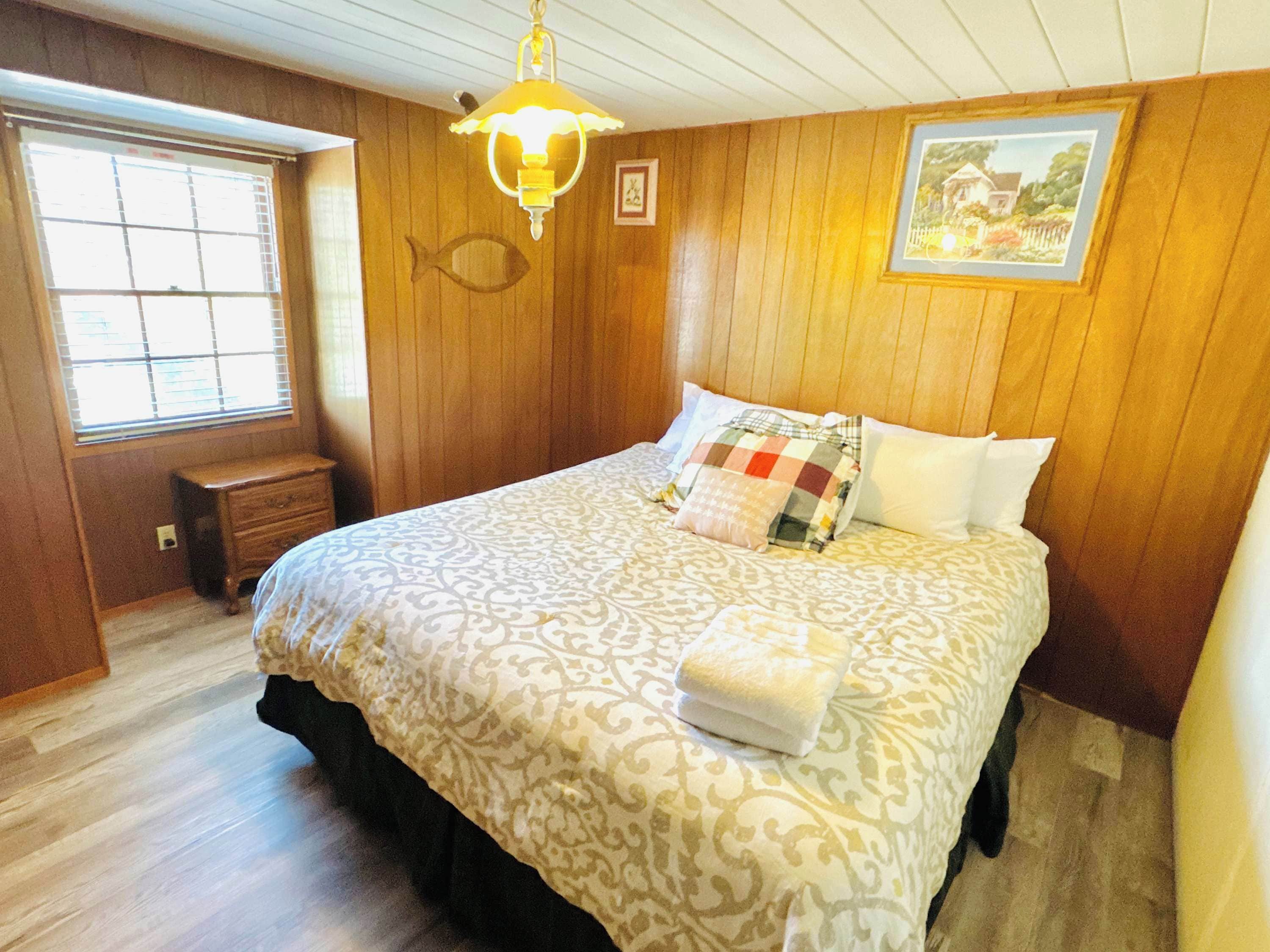 A bedroom with a bed, a nightstand, a window, and a painting on the wall.