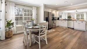 Une cuisine moderne avec des meubles blancs, un réfrigérateur en acier inoxydable et un coin repas comprenant une table et des chaises en bois.