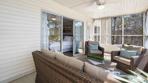 Un patio couvert aménagé avec des meubles en osier, un lit doté de portes coulissantes en verre et une vue sur les arbres.